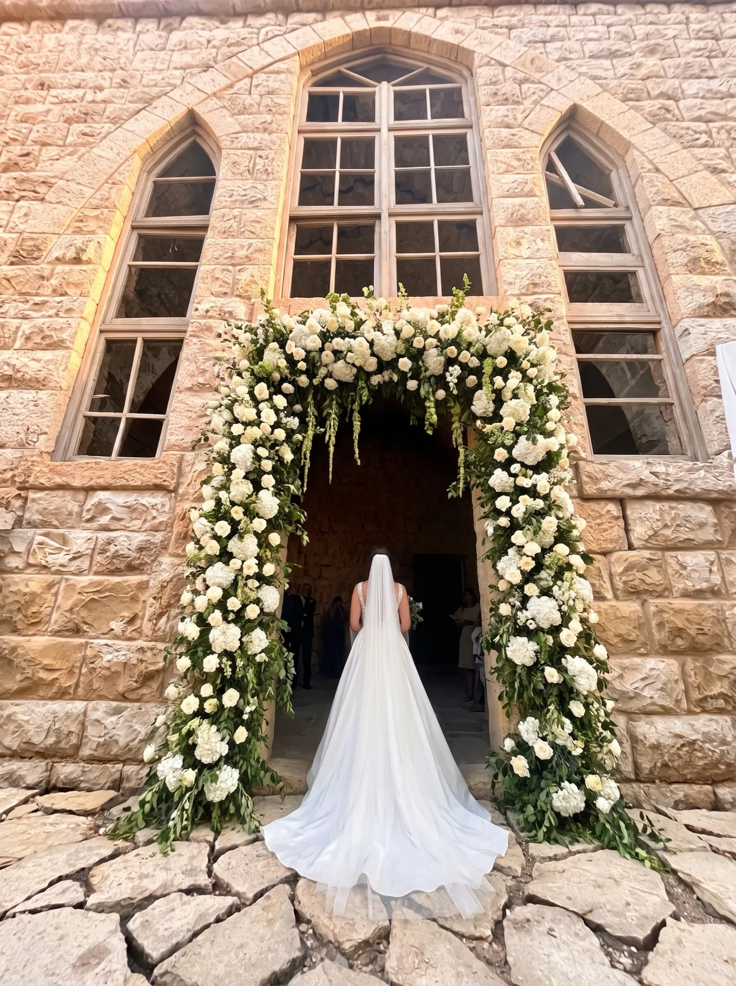 Styled visualisation of the same doorway framed in white roses with a bride walking through