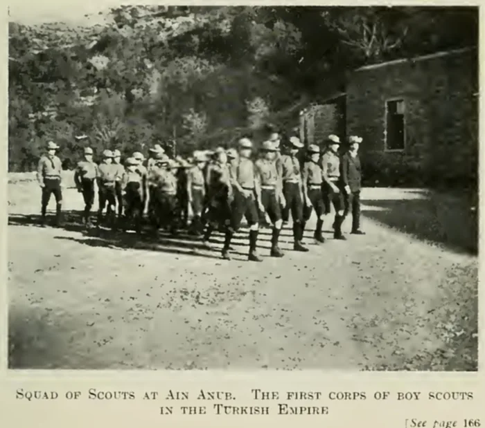 Archival photograph of a squad of uniformed boy scouts marching in the school grounds at Ain Anub