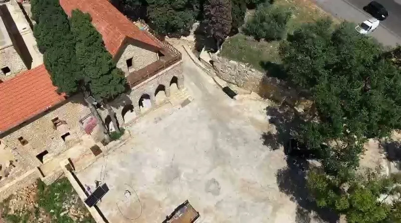 Aerial view of Qasr Noun in Ain Anub: tiled roofs, the arched arcade and an open stone courtyard bordered by trees